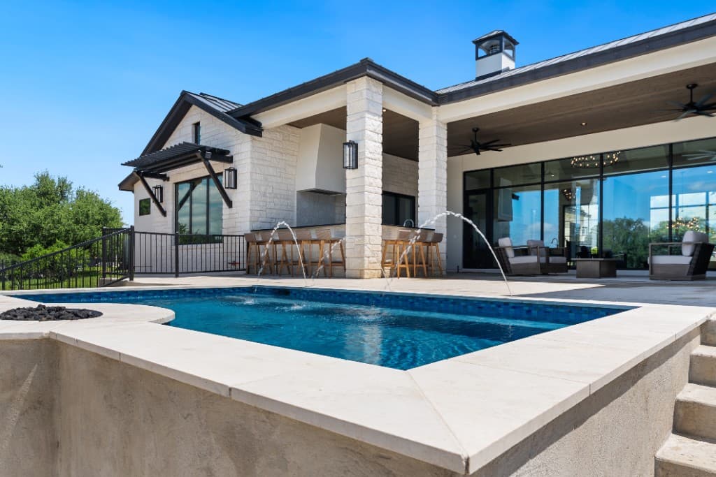 Raised rectangular pool with blue mosaic tile, fire feature, and outdoor kitchen