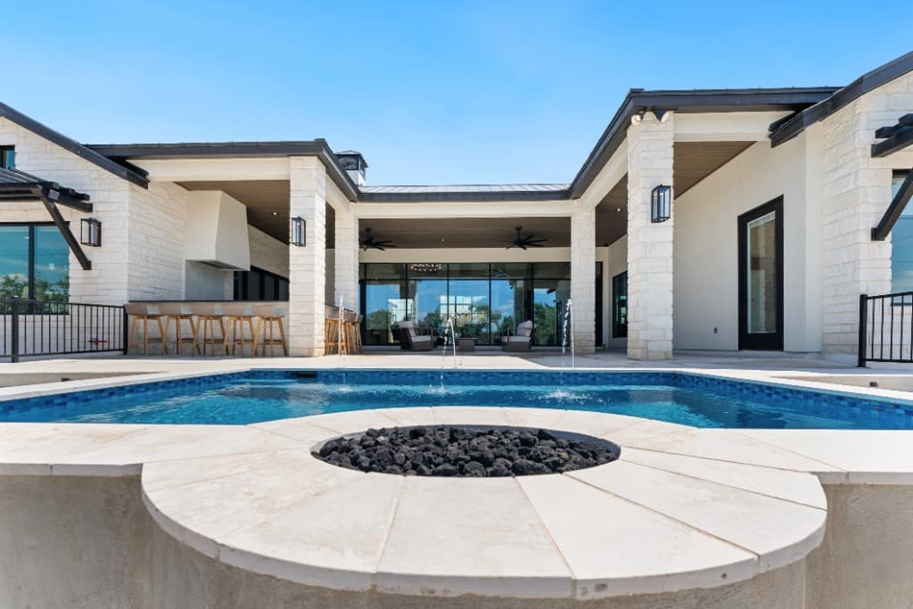 Luxury pool with fountain jets and a Texas Hill Country stone home beyond