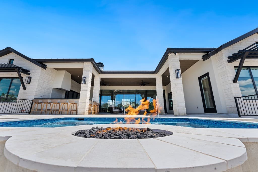 Modern backyard pool with deck jets, stone coping, and covered patio